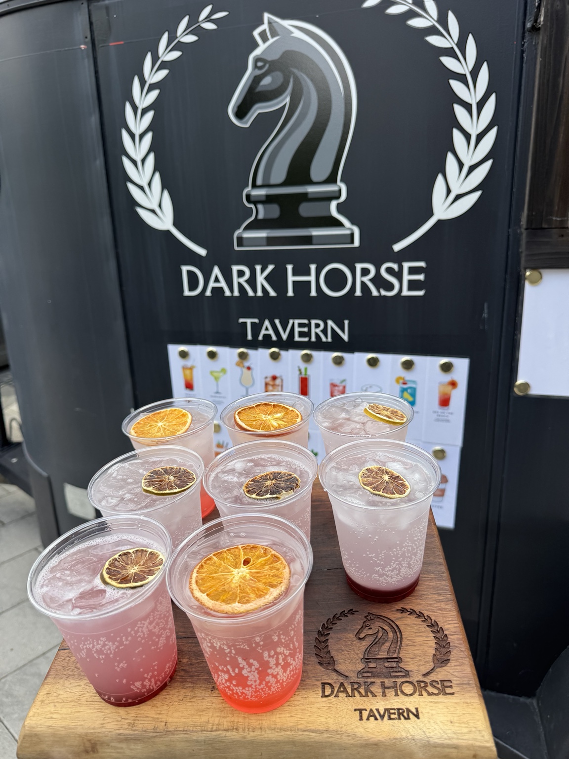 Pink citrus-garnished cocktails on a branded Dark Horse Tavern serving board