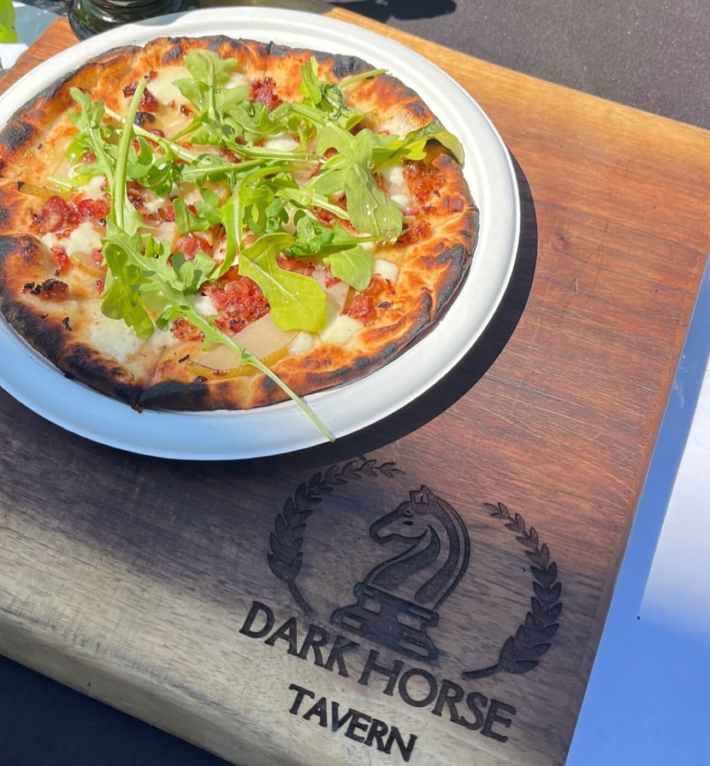 Flatbread pizza topped with arugula on a Dark Horse Tavern serving board